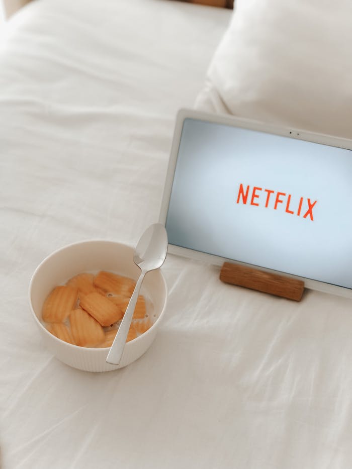 Tablet displaying Netflix beside a bowl of snacks on a cozy bed setting.